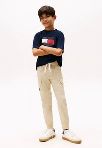 Laivastonsininen T-paita, jossa punainen, valkoinen ja sininen vaakasuora kuvio; beiget taskulliset cargohousut, joissa kiristysnyöri; valkoiset lenkkarit beigen yksityiskohdilla.