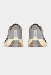 Par de zapatos deportivos grises vistos desde atrás, con medias suelas de color beige claro, suelas exteriores marrones translúcidas y lengüetas reflectantes en el talón.