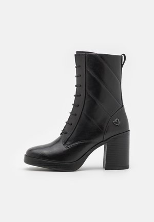 Bottine noire en cuir avec talon bloc, lacets à l'avant, design matelassé sur le côté et petit détail en forme de cœur près du talon.
