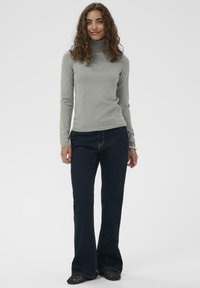 Svetilka iz svetlo sive barve z visokim ovratnikom v prilegajočem se kroju, kombinirana s temno modrimi širokimi jeans hlačami. Svetilka ima dolge rokave in rebrast rob.
