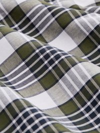 Vågig tyg med ett rutmönster i grönt, svart, grått och vitt, som visar detaljerad vävtexture och korsande linjer.