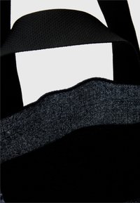 Czarna torba tote z teksturowanym materiałem na górze i gładkim czarnym tworzywem poniżej. Posiada mocne czarne uchwyty. Prosty, funkcjonalny design.