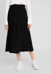 Gonna nera midi con una cintura elastica arricciata, tessuto fluido e una consistenza liscia. Abbinata a sneakers bianche con zeppa.