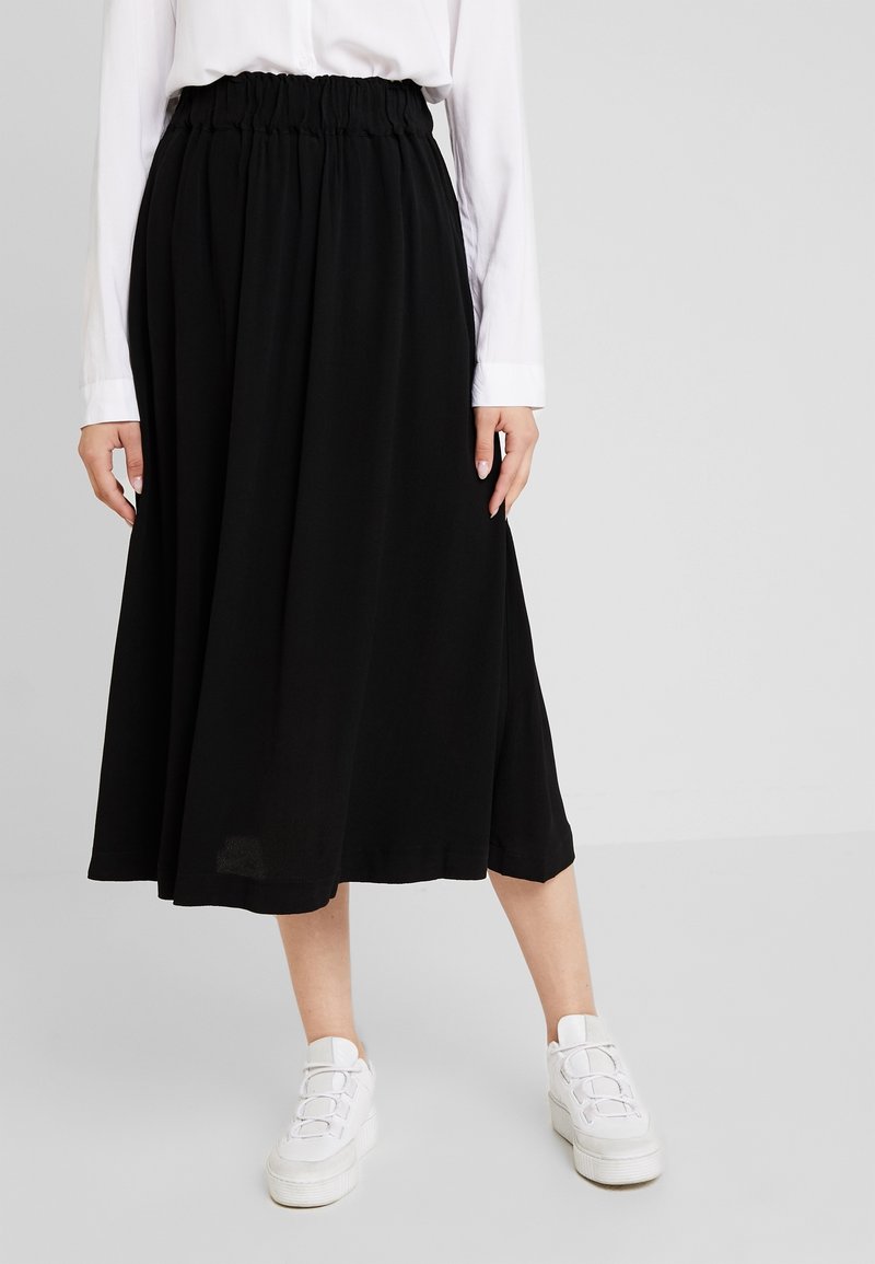 Sorte midi nederdel med en samlet elastisk talje, flydende stof og en glat tekstur. Sammen med hvide platform sneakers.