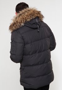 Czarna pikowana kurtka puchowa z odpinanym kapturem wyłożonym brązowym futerkiem, poziomy pikowany wzór, dwie boczne kieszenie oraz regulowany sznurek przy szyi.