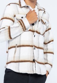 Rutigt skjortjacka i vitt och beige med bruna ränder, med dubbla bröstfickor, knapplåsning och ett mjukt texturerat tyg.