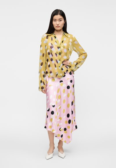 Διαφανές κίτρινο μπλουζάκι με πολύχρωμες πουά, συνδυασμένο με ροζ ασύμμετρη φούστα με μαύρες και χρυσές λεπτομέρειες.