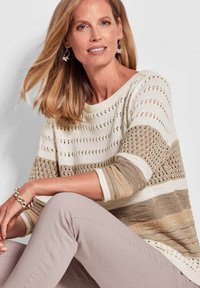 Maglione a maglia in tonalità crema e beige con motivi a punto aperto, colletto rotondo e maniche a tre quarti, abbinato a pantaloni beige chiaro.