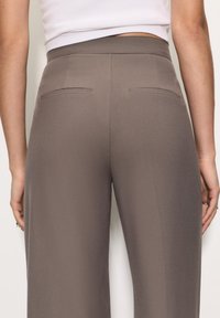 Szürke, testhez simuló nadrág sima textúrával, két hátsó zsebbel és magas derékkal, hátulról nézve.