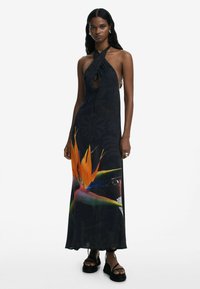 Maxi dress in dark fabric featuring a halter neckline and a cutout detail. Prominent flower print in orange and green, with textured accents.