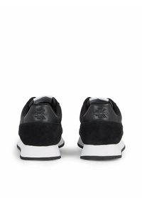 Baskets noires en cuir et suède, avec une semelle intermédiaire blanche, un bout arrondi, et le logo Calvin Klein sur le talon.