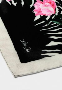 Écharpe florale en motif zèbre noir et blanc, ornée de fleurs roses, en tissu doux, avec des coutures noires et une signature blanche dans un coin.