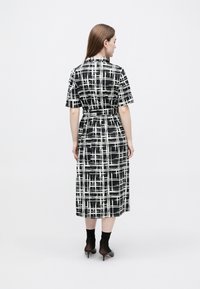 Rochie în carouri alb-negru, cu mâneci scurte, talie cu curea și lungime midi, realizată dintr-un material neted. Are decolteu cu rever.