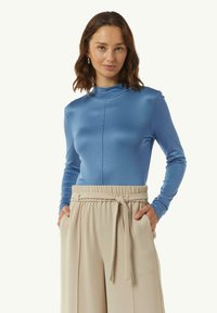 Lichtblauw lang mouwtop met een hoge halslijn en een zachte textuur, gecombineerd met beige hoog-taille broeken met een knoopdetail in de taille.