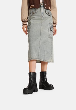 Gonna midi in denim blu sbiadito con tasche a toppa, abbinata a stivali alla caviglia con suola spessa neri, dotati di dettagli a cinghia e finitura testurizzata.