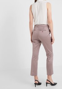Pantaloni rossi a fantasia con una vestibilità slim, realizzati in un tessuto testurizzato e con vita media. Abbinati a sandali neri con tacco.