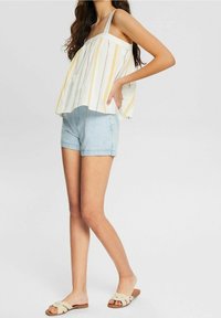 Débardeur blanc avec des rayures jaunes et rouges, associé à un short en denim bleu clair et des sandales beige à enfiler avec des lanières croisées.