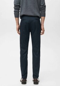 Marinblå byxor med en slät tygfinish, slim fit-design och två bakfickor, som bärs med en grå tröja och bruna skor.