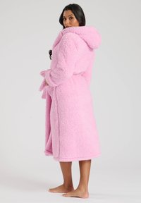 Roa rosa e soffice con cappuccio, maniche lunghe e vita con cinturino. Presenta un'esterno testurizzato e coccoloso e orlo a lunghezza ginocchio.