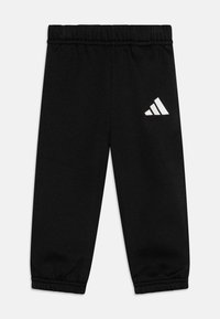Pantalons de survêtement noirs en tissu doux, avec une taille élastique et des chevilles resserrées, portant un logo blanc Adidas sur le bas de la jambe gauche.