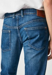 Jeans de mezclilla azul oscuro con corte recto, que cuentan con dos bolsillos traseros, costuras en contraste y una etiqueta de cuero marrón en la cintura.