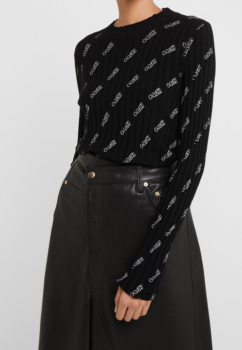 Haut noir à manches longues côtelé avec logo blanc imprimé, col rond et tissu texturé. Associé à une jupe en cuir noire taille haute.