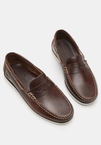 Brown leather loafers with a slip-on design, featuring decorative stitching along the edges and a contrasting white rubber sole.