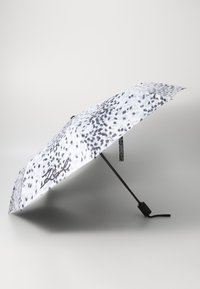 White umbrella with black spotted pattern. Features a black handle and a strong metal frame for stability. Signature on one side.