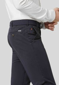 Chino navy à la texture lisse, avec une ceinture tressée, fermeture à bouton et une étiquette logo. Comprend des poches latérales et des couleurs d'accentuation subtiles.