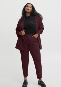 Blazer bordeaux et pantalons fuselés assortis portés sur un top noir à imprimé léopard. Le tissu est lisse avec un léger brillant. Des chaussures noires complètent la tenue.