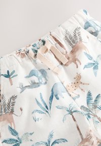 Shorts en coton avec un fond crème clair, arborant un motif ludique de dinosaures et de feuilles de palmier dans des tons doux de bleu et de brun. Cordon de serrage ajustable.
