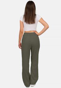 Olijfgroene, lichte broek van een gestructureerde stof. Heeft een elastische tailleband en een lengtemaat die de enkels bereikt, gecombineerd met een witte cropped top.