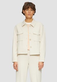 Veste courte de couleur crème avec un col, deux poches avant et fermeture à boutons. Tissu léger avec une texture lisse.