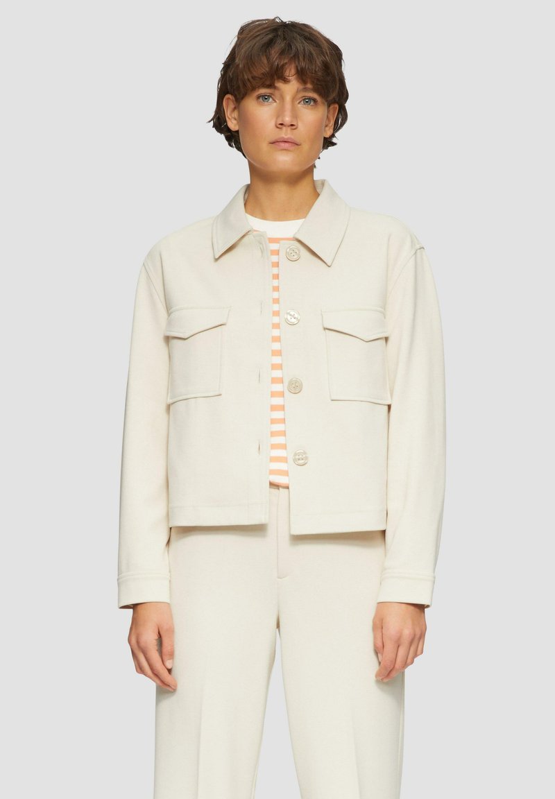 Veste courte de couleur crème avec un col, deux poches avant et fermeture à boutons. Tissu léger avec une texture lisse.
