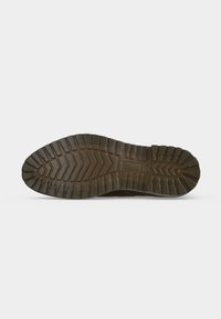 Semelle de chaussure marron foncé avec des motifs de bande de roulement profonds en zigzag et rectangulaires sur un fond clair uni.