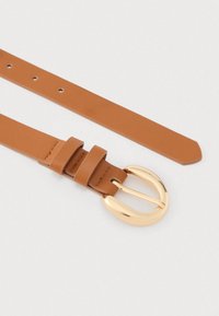 Ζώνη από μαλακό δέρμα σε ταμπά χρώμα με χρυσή αγκράφα διπλής ακίδας. Διαθέτει τρεις ρυθμιζόμενες τρύπες και λεία υφή. Τα άκρα είναι κομμένα ίσια.