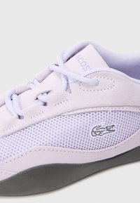 Világoslila sneaker velúr és hálós anyagból, szürke gumitalppal, fűzőkkel és egy kicsi, hímzett logóval az oldalon.