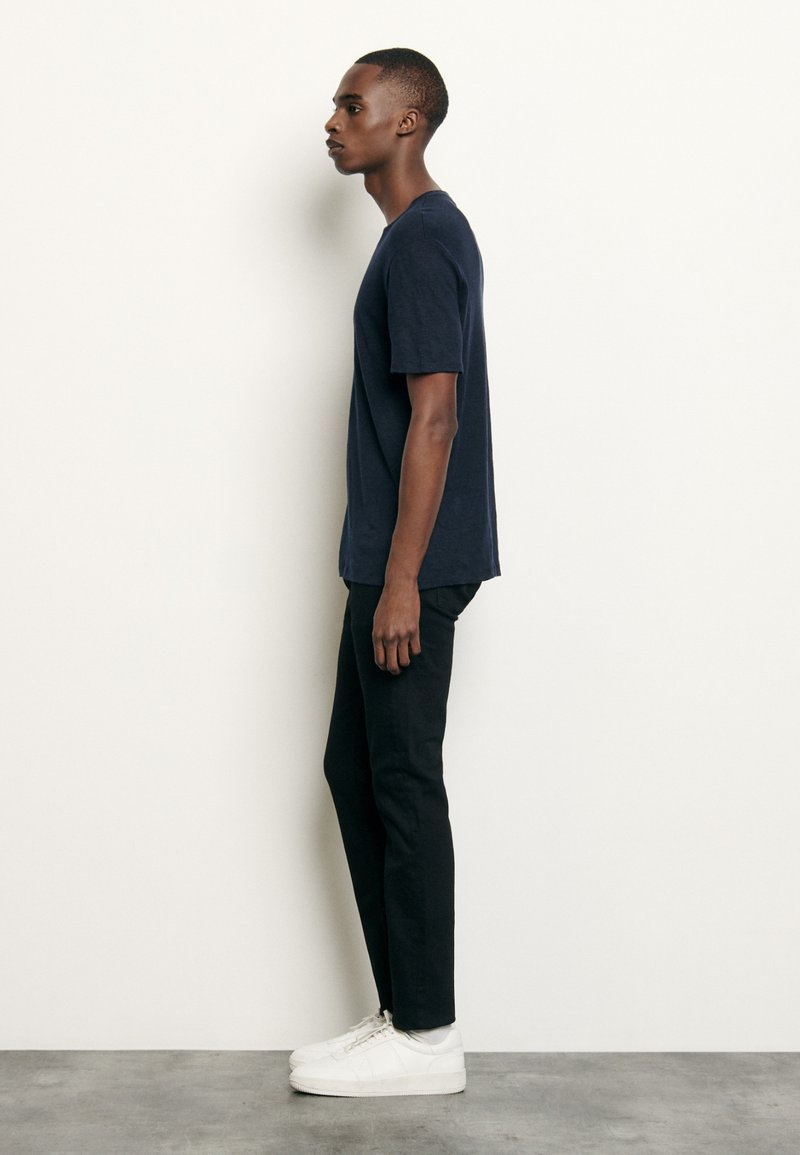 Camiseta de manga corta azul marino combinada con pantalones negros y zapatillas blancas. La camiseta tiene un corte estándar y un cuello redondo.