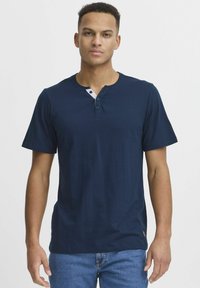 Tamno plava kratki rukav henley majica od mekanog materijala. Ima tri dugmeta i kontrastne bijele detalje oko vrata.