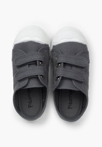 Zapatos de lona gris con suelas de goma blanca, que cuentan con dos tiras de Velcro y costuras decorativas para un detalle adicional. El forro interior es de color gris.