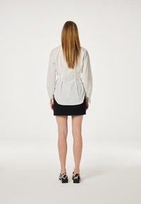 Witte button-up blouse met lange mouwen, gecombineerd met een zwarte corduroy mini rok. Sch footwear met een luipaardprint en blokhakken.