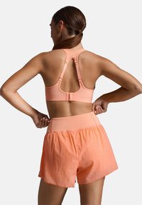 Sportbeha met een racerback ontwerp in gestructureerd lichtroze, vastgemaakt met een haakje. Gecombineerd met lichte, luchtige koraalkleurige shorts.