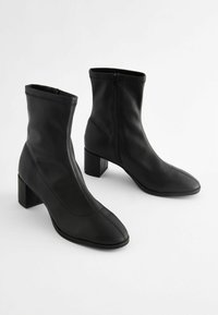 Svarta ankelskor i slätt skinn med en elegant design, fyrkantiga klackar, sidodragkedjor och spetsiga tår. Strukturerad sömsyn.