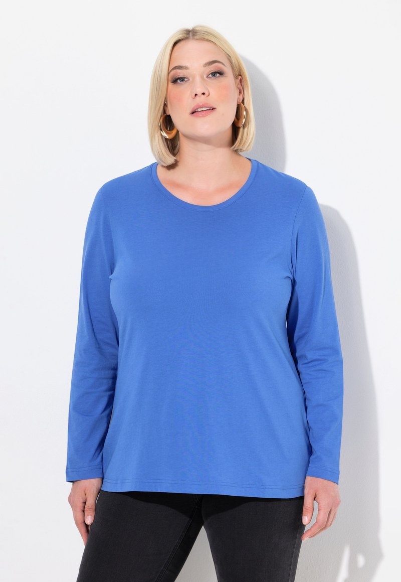 Langärmliges blaues T-Shirt aus weichem Stoff mit rundem Halsausschnitt, entspannter Passform und einfachem Design, kombiniert mit dunklen Jeans.