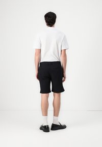 Black shorts with a rolled hem, paired with a white polo shirt. The shorts feature a classic fit and back pockets. Black shoes complete the look.