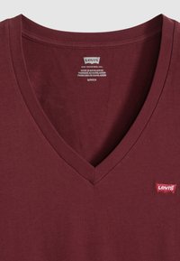 Μπορντό μπλουζάκι V-neck Levi's με μικρό κόκκινο λογότυπο Levi's στο στήθος και εκτυπωμένες λεπτομέρειες μεγέθους και κατασκευής στο εσωτερικό του γιακα.