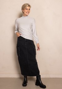 Light gray, textured long-sleeve top with a high neck; paired with a black denim maxi skirt featuring deep side pockets; worn with black ankle boots.