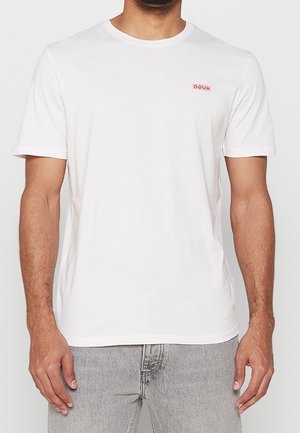 Weißes Baumwoll-T-Shirt mit kurzen Ärmeln, Rundhalsausschnitt und kleinem roten Logo auf der linken Brust. Kombiniert mit hellgrauen Jeans.