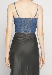 Farkkuinen lyhyt toppi ohuilla olkaimilla; siinä on rypytetty takaosa. Yhdistetty mustaan satiinihameeseen, jonka vyötärönauha on osittain näkyvissä.