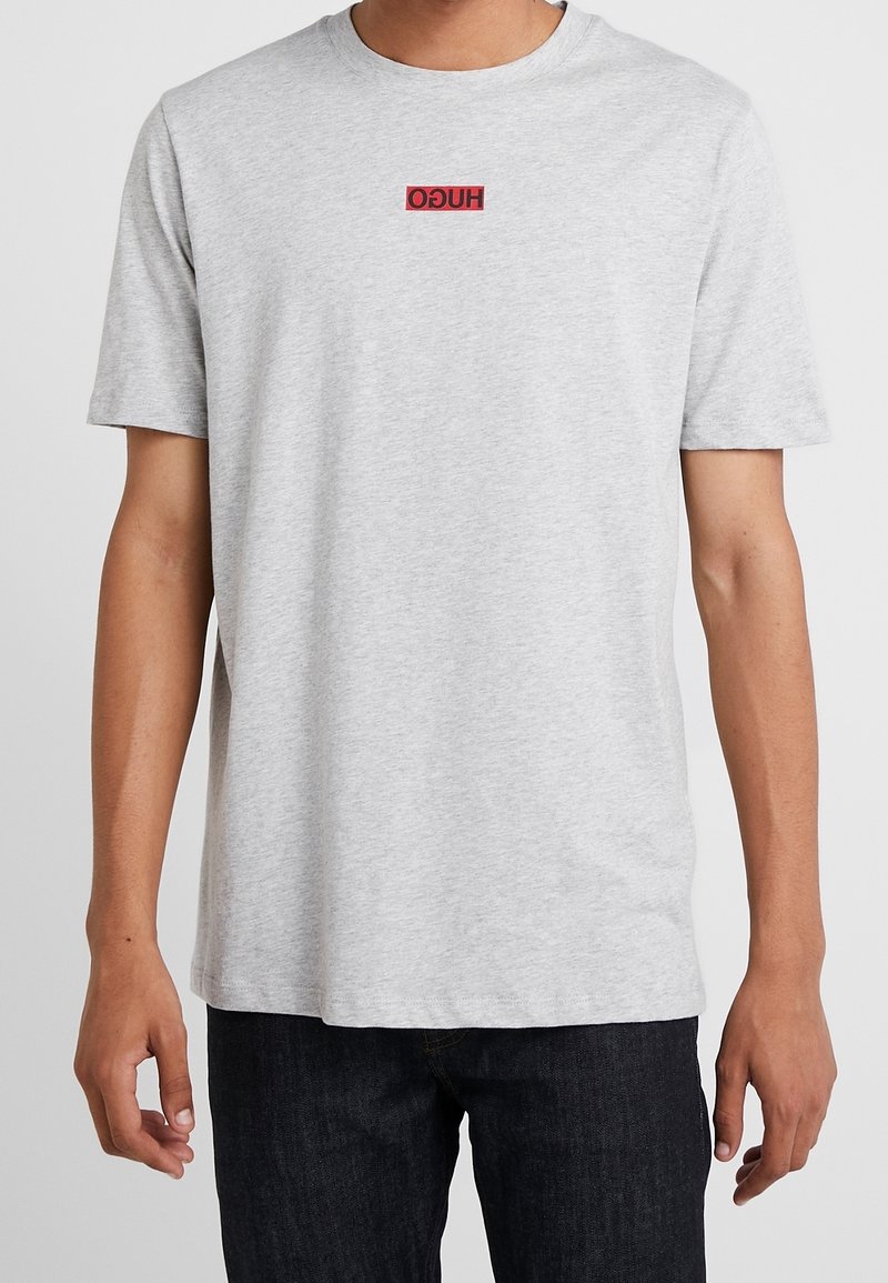 Grijs katoenen T-shirt met korte mouwen, voorzien van een klein rood "HUGO"-logo in het midden van de borst. Simpel, klassiek design met ronde hals.